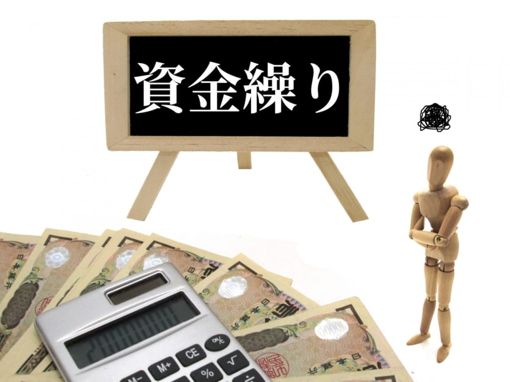 「資金繰り」の文字と電卓とお金を前に悩む人