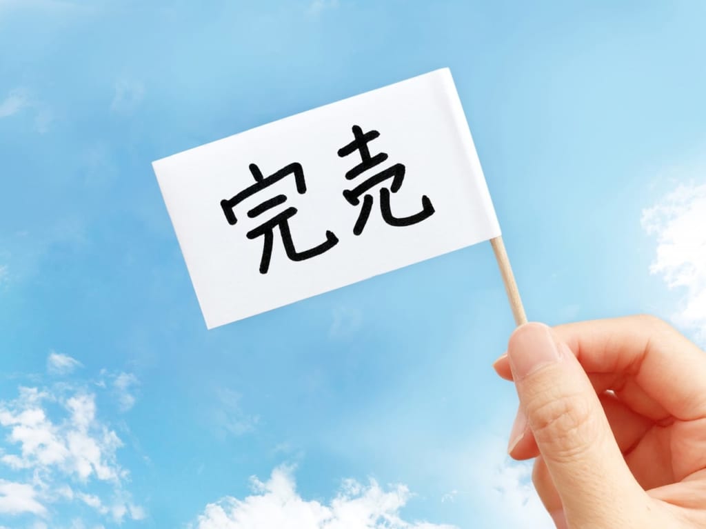「完売」と書かれた旗を持つ人の手