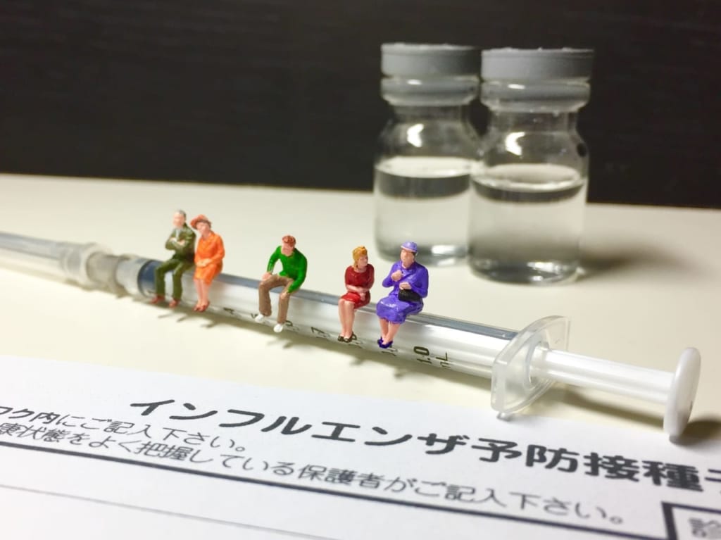 インフルエンザ予防接種の問診票と注射器の上に腰掛ける人々
