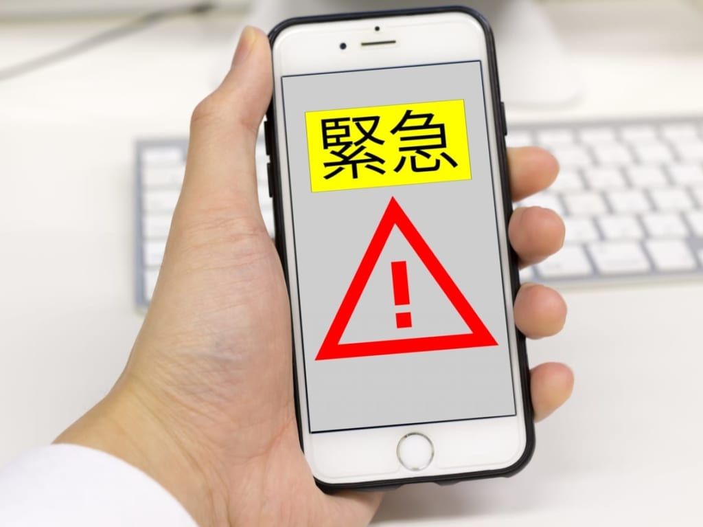 「緊急」と表示されたスマートフォンを持つ人の手