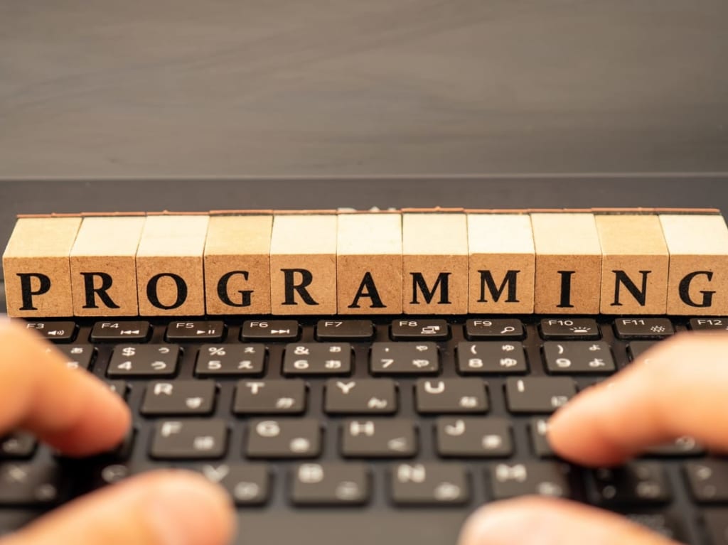 「programming」と書かれた木製のキューブと、キーボードを叩く人の指