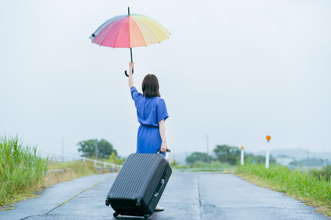 スーツケースを手に、カラフルな傘を掲げる女性の後ろ姿
