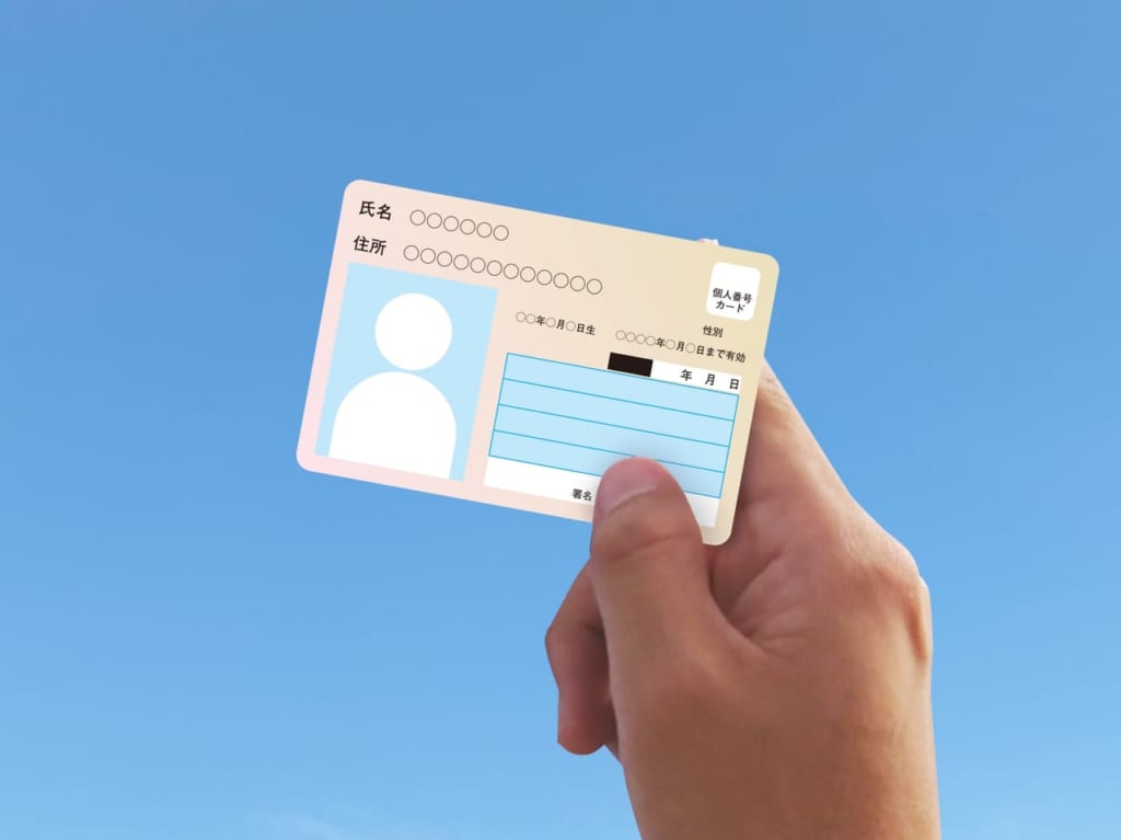 青空にマイナンバーカードを掲げる人の手